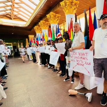 People protest in a corridor with two men with amputated legs hold a sign that says "Look what AP landmines will do to your people."