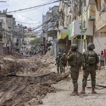Israeli soldiers look on as Palestinian men and women carry their belongings on May 2, 2025 amid ongoing Israeli military operations and demolition of homes in Tulkarem refugee camp. Israeli forces had emptied the refugee camp of its inhabitants weeks prior.