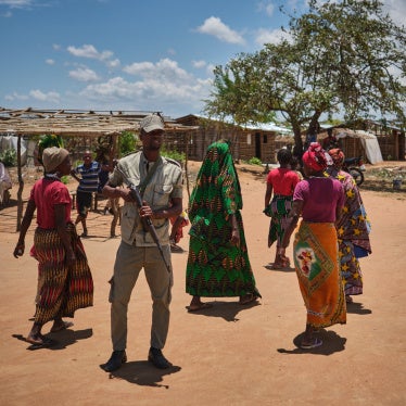 A police officer patrols in front of women in a shelter for internally displaced people