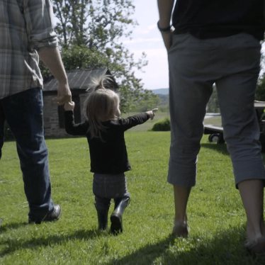 A young child stands between her parents in their garden, pointing into the distance