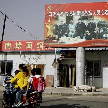 A Uighur woman picking up school children rides past a picture showing China's President Xi Jinping joining hands with a group of Uighur elders at the Unity New Village in Hotan, in western China's Xinjiang region. 